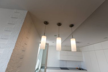 Mutfak adasının üstünde, pencerenin altında, bar tabureleri olan beyaz lambalar.