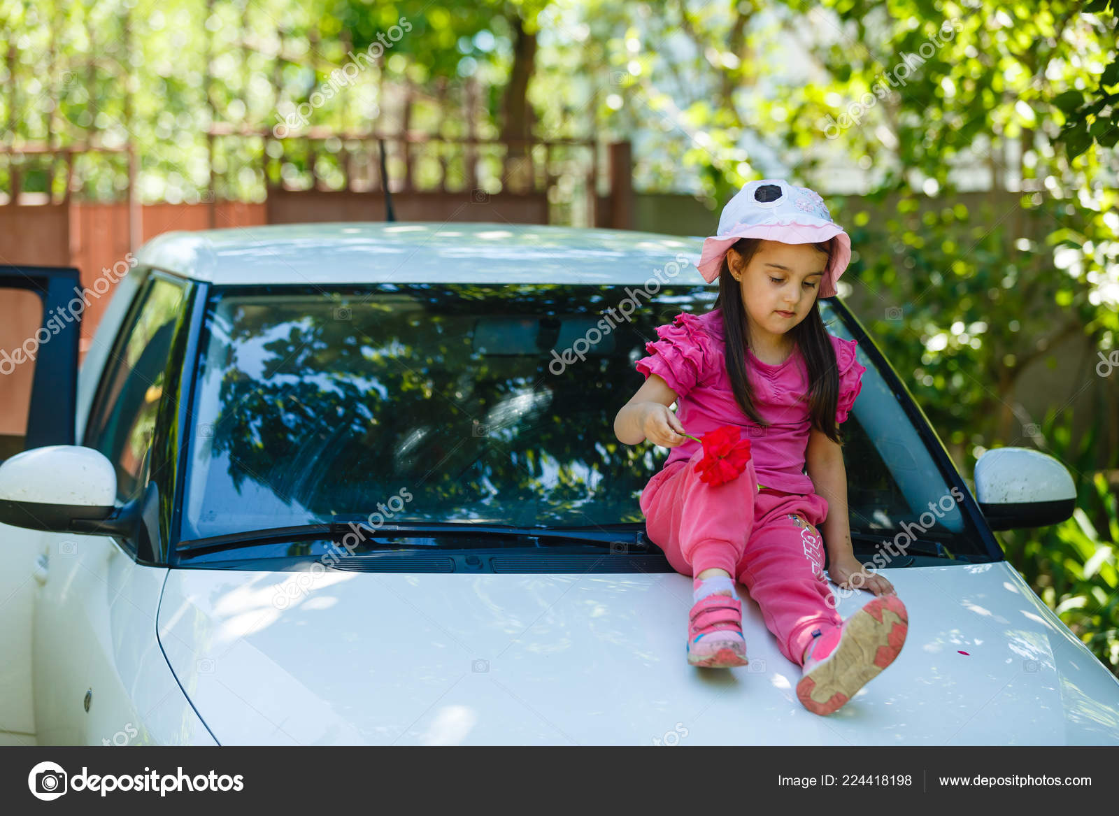 Araba kaputunda oturan küçük mutlu kız 