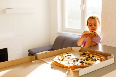 Güneşli mutfakta lezzetli pizza yiyen aç küçük kız portresi