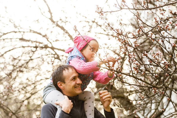 Father with little daughter in arms having fun in  blooming garden