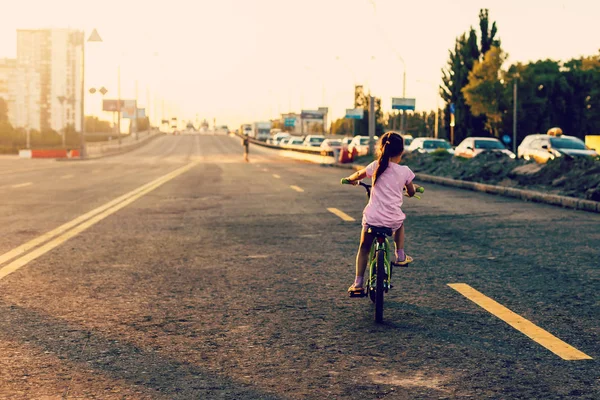 日没時に道路に自転車に乗って小さなブルネットの女の子 — ストック写真