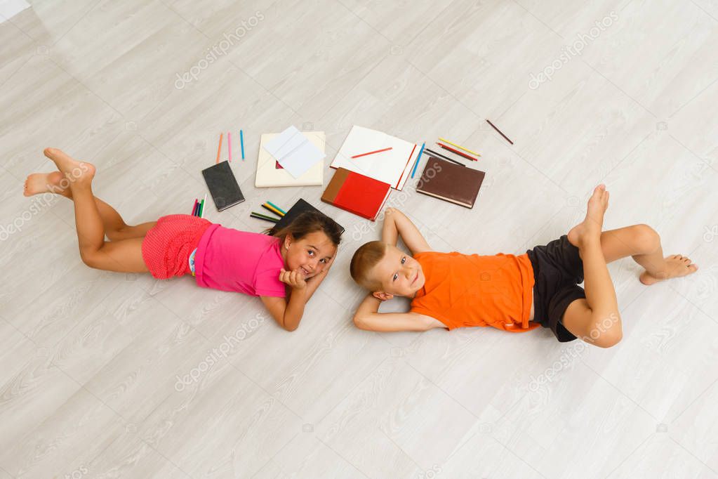 Top view of little boy and girl lying near books and toys on floor 