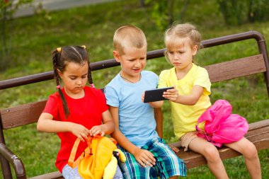 Üç mutlu çocuk parkta bankta smartphone ile oynamak 