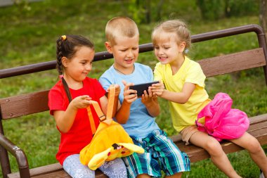 Üç mutlu çocuk parkta bankta smartphone ile oynamak 