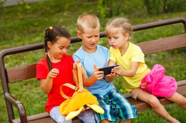 Üç mutlu çocuk parkta bankta smartphone ile oynamak 