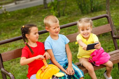 Üç mutlu çocuk parkta bankta smartphone ile oynamak 