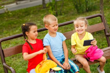 Üç mutlu çocuk parkta bankta smartphone ile oynamak 