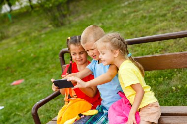 Üç mutlu çocuk parkta bankta smartphone ile oynamak 