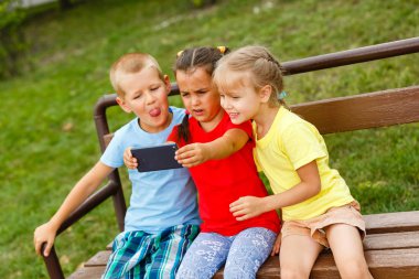Üç mutlu çocuk parkta bankta smartphone ile oynamak 