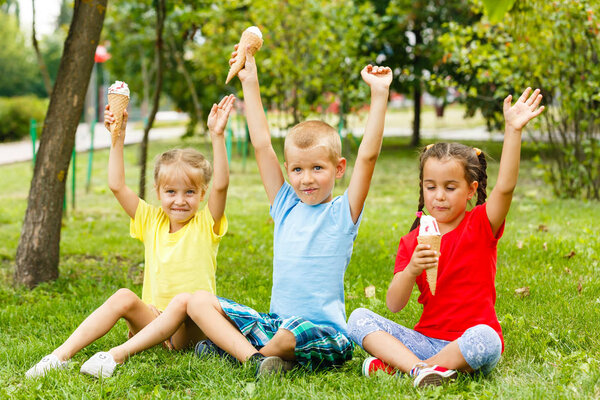 Little children sitting on green grass and eating ice-cream 