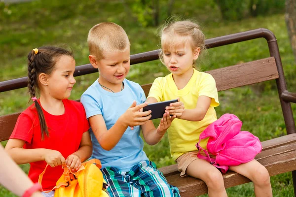 Trzy Szczęśliwe Dzieci Bawiące Się Smartphone Ławce Parku — Zdjęcie stockowe