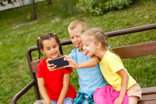 Drei Glückliche Kinder Spielen Mit Smartphone Auf Bank Park — Stockfoto