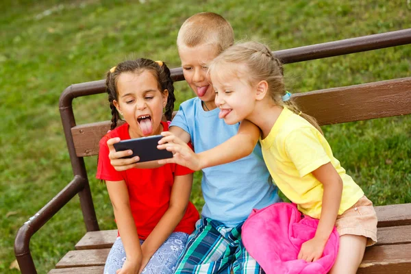 Tres Niños Felices Jugando Con Teléfono Inteligente Banco Parque —  Fotos de Stock