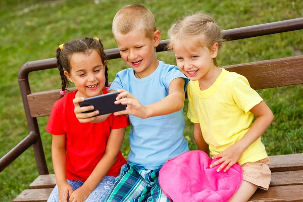 Tres Niños Felices Jugando Con Teléfono Inteligente Banco Parque —  Fotos de Stock