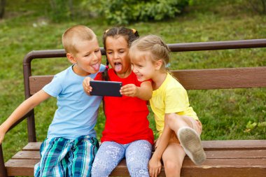 Üç mutlu çocuk parkta bankta smartphone ile oynamak 
