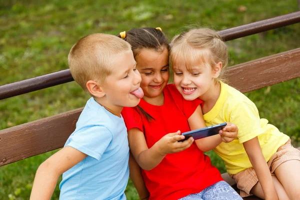 Tres Niños Felices Jugando Con Teléfono Inteligente Banco Parque — Foto de Stock