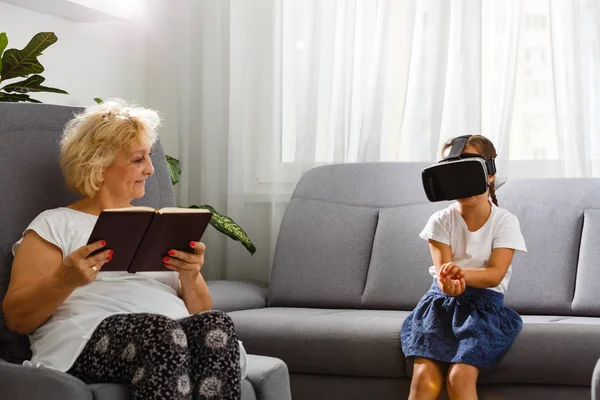 old woman reading book and girl playing with VR goggles