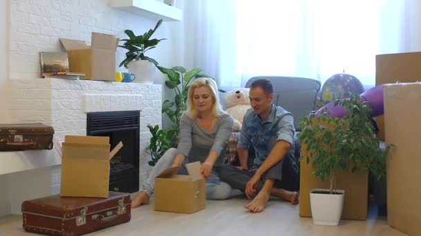 Happy Young Couple Opening Cardboard Box Looking While Sitting Floor — Stock Video