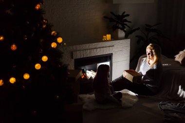 Anne ve kızı daughterspending zaman katta şömine ve Noel ağacı karanlık oturma odasında otururken 