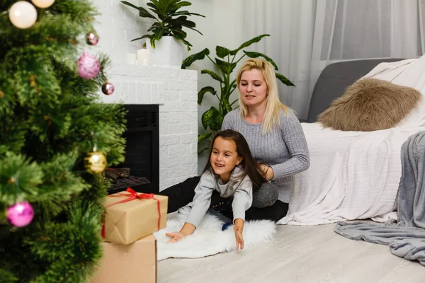 リビング ルームでクリスマス ツリーと暖炉の近くの床に座っている娘の娘を持つ母 — ストック写真