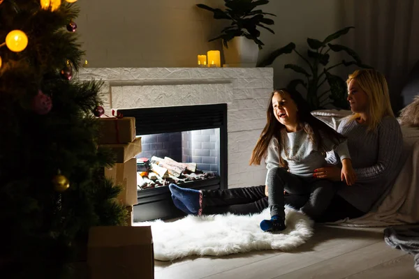 母亲和女儿在黑暗的客厅里坐在壁炉附近的地板上 在圣诞树上呆着 — 图库照片