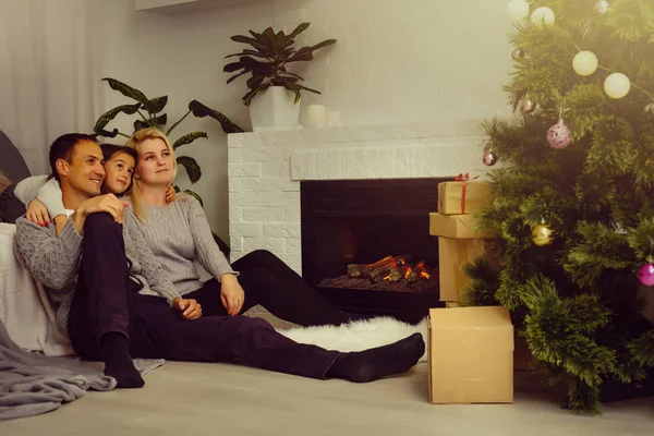 Family sitting on floor near fireplace and Christmas tree at living room