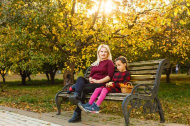 Anne ve kızı sonbahar parkında bir bankta.