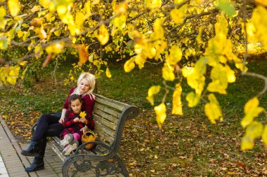 Mutlu anne ve kız sonbahar parkında bir bankta kucaklaşıyorlar.