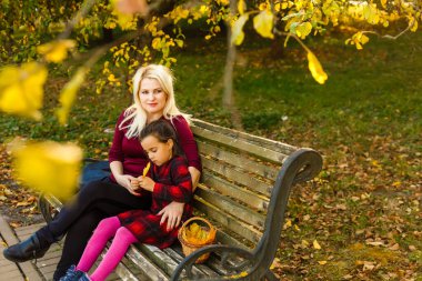 Anne ve kızı sonbahar parkında bir bankta.