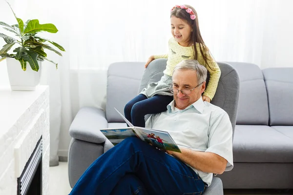 自宅のソファの上で祖父と孫娘 おじいちゃんと子供たちはアルバムで写真を見ている — ストック写真