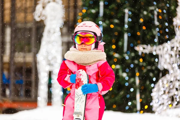 小女孩带着护目镜和头盔参加寒假 站在户外滑雪板后面看着相机 微笑着兴奋的特写模糊的背景 — 图库照片