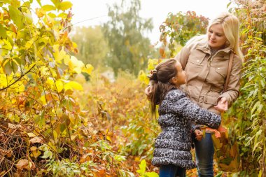 Anne ve kızı sonbahar ormanında yürüyor.