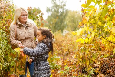 Genç anne sonbahar parkında kızıyla oynuyor.