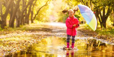 Yağmurlu bir günde su birikintisinde koşan lastik çizmeli küçük kız.