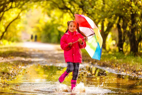 ピンクのジャケットとゴムブーツで非常にかわいい女の子は雨の日に水たまりの上にジャンプしています — ストック写真