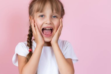 Uzun saçlı, beyaz tişörtlü, pembe arka planda gülümseyen güzel sarışın kız.