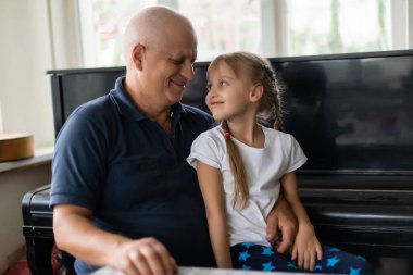 Komik iki kişinin fotoğrafı. Yaşlı büyükbaba ilgilenen küçük torun kanepeye oturmuş güzel bir hikaye anlatıyor. Ev karantinası, güvenlik, modern tasarım iç mekan.