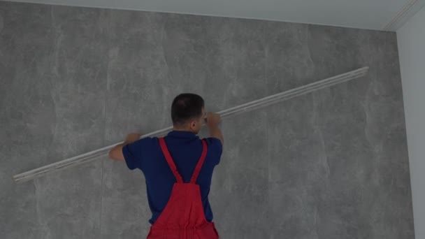 Vista lateral del hombre caucásico muscular con una amplia espátula alinea la pared, pintor barbudo aplica masilla, preparación para la pintura en la habitación, espacio de copia. — Vídeo de stock