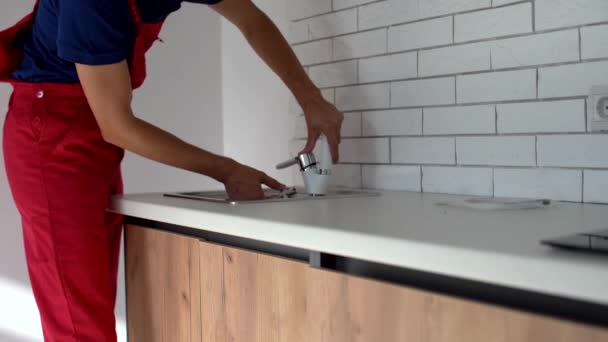 En professionell rörmokare, i uniform, säkerställer kvaliteten på installationen av kranen i köket. Installera en ny kran på tvättställ för kök — Stockvideo