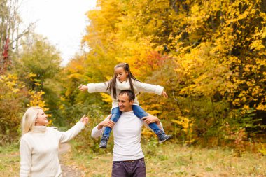 Sonbahar parkında güzel bir aile fotoğrafı, güzel bir kızı olan genç bir aile dışarıda oynuyor, sonbaharda arka bahçede eğleniyor, mutlu bir aile sonbaharda doğanın tadını çıkarıyor.