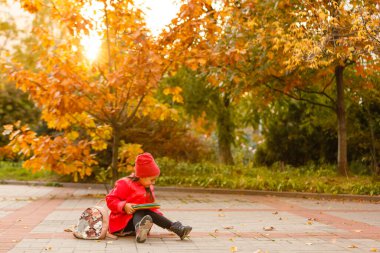 Elinde kitapla ilkokul öğrencisi. Açık hava binasının yakınında sırt çantalı bir kız. Dersler başlıyor. Sonbaharın ilk günü.