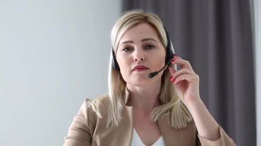 Kendine güvenen kadın ofis çalışanı kulaklık takıyor ve dizüstü bilgisayara bakıyor. Genç iş kadını müşteri hizmetleri müdürü uzaktan iletişim kuran webcam ile konuşuyor..