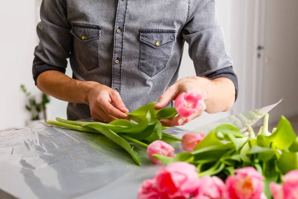 Flowers delivery shop. Florist creating order, making spring bouquet. Male make bouquet using tulips