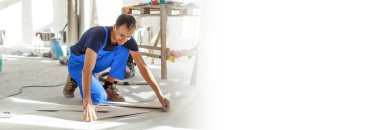 Üstad iş kıyafetleri giyiyor, fayans döşemeyi kontrol ediyor, bina seviyesini kullanıyor, ayarlamalar yapıyor, profesyonel onarım işi yapıyor.