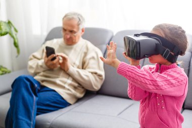 Torunu, büyükannesi ve büyükbabasıyla evdeki oturma odasında sanal gerçeklik kulaklığı kullanıyor.