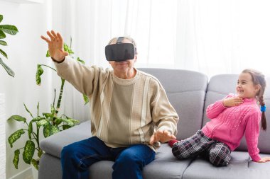 Torunu, büyükannesi ve büyükbabasıyla evdeki oturma odasında sanal gerçeklik kulaklığı kullanıyor.