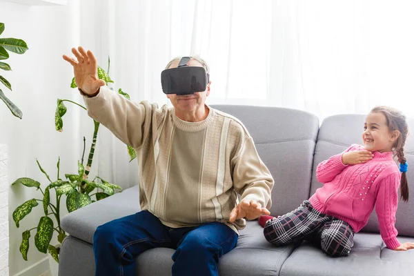 Torunu, büyükannesi ve büyükbabasıyla evdeki oturma odasında sanal gerçeklik kulaklığı kullanıyor.