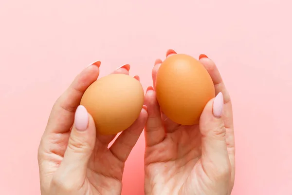 Two eggs In hand holding on a pink background