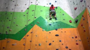 Küçük bir kız kayalık bir spor salonunda duvara tırmanıyor.