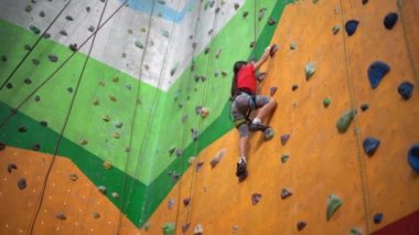 Küçük bir kız kayalık bir spor salonunda duvara tırmanıyor.